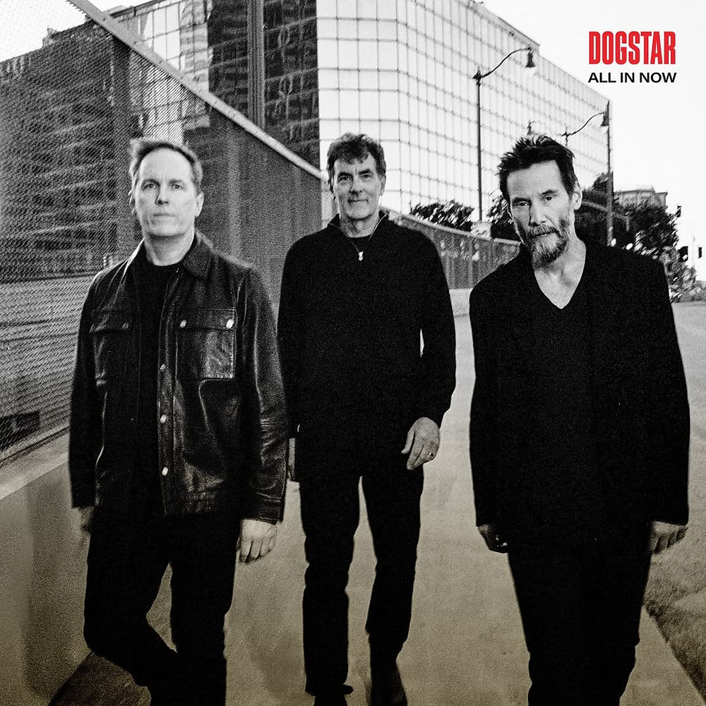Three men walk casually on a city street, wearing dark clothing. Background features glass buildings and fencing. Text: "DOGSTAR ALL IN NOW".