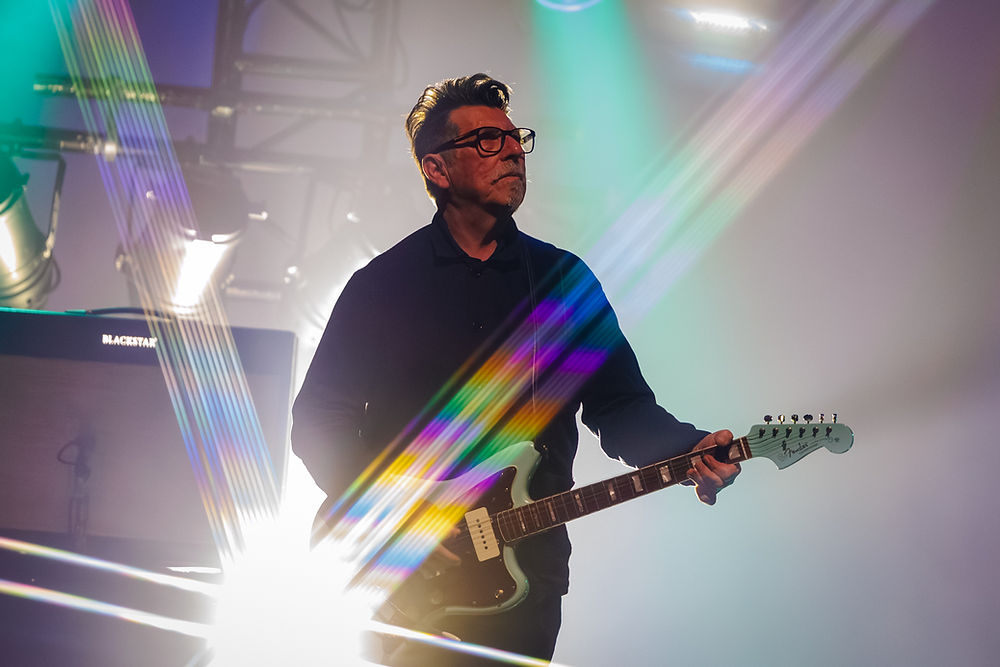 Man playing electric guitar on a smoky stage with rainbow lens flares and a Blackstar amp behind him.