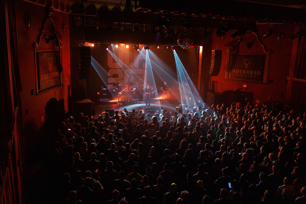 Band performs on stage at Buckhead Theatre. Crowd watches under colorful lights. Energetic concert atmosphere fills the ornate venue.