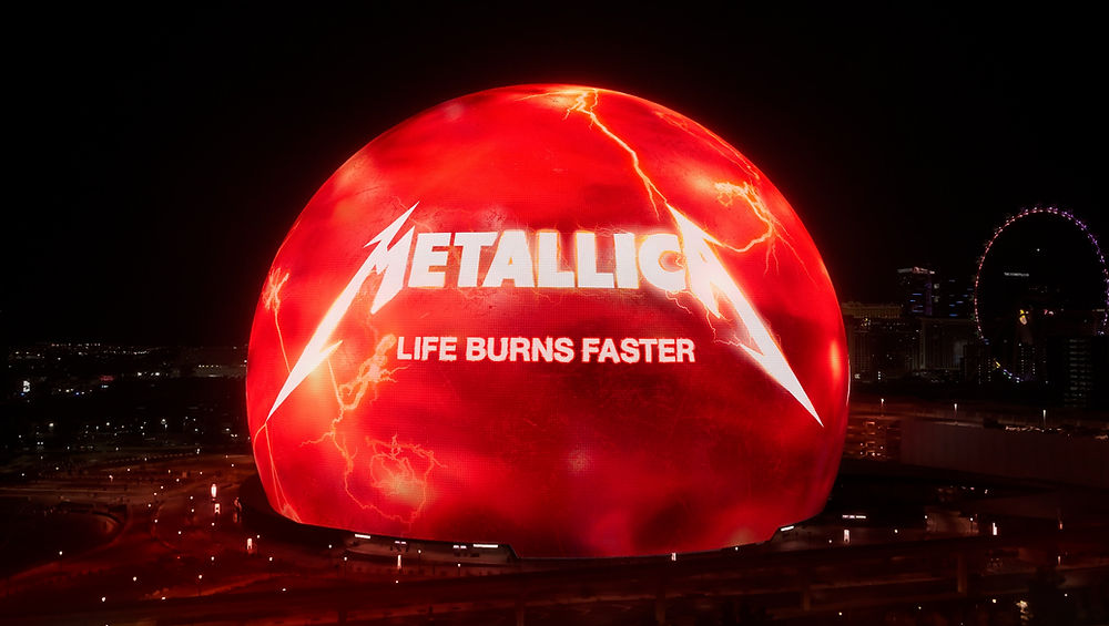 A large glowing red sphere displays "Metallica" and "Life Burns Faster" in bright letters, set against a nighttime cityscape background.